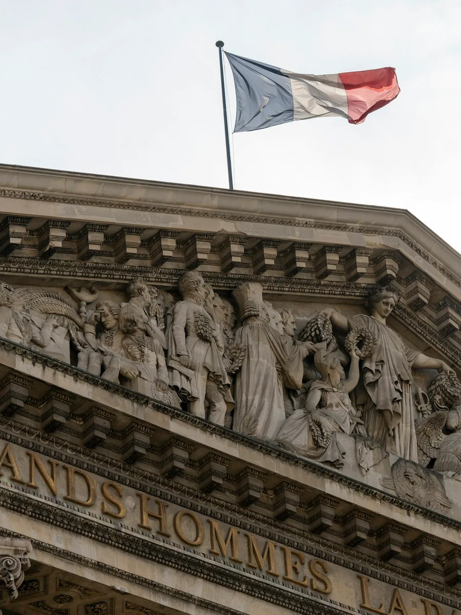 Un drapeau français flotte au-dessus du fronton sculpté du Panthéon, à Paris.