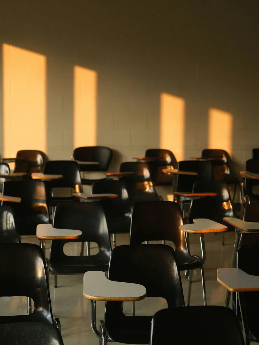 Une salle de classe vide, chaises et tablettes alignées, dans la lumière rasante du soleil.