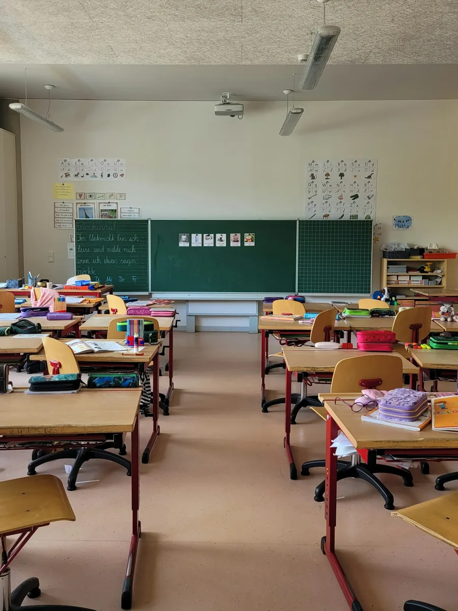 Salle de classe d'école primaire vide, avec ses tables, ses chaises et un tableau vert