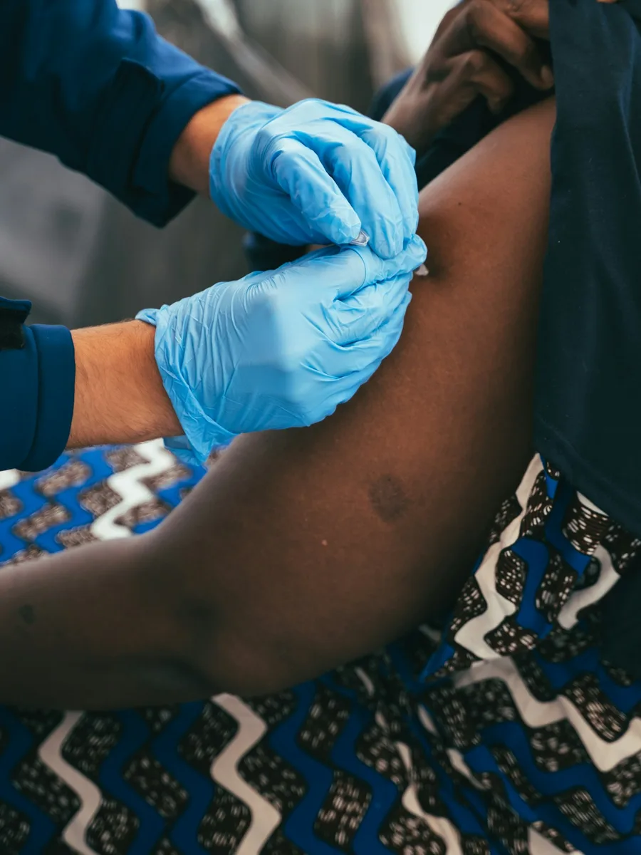 Mains gantées de bleu d’un soignant qui injecte un vaccin dans le haut du bras d’une personne