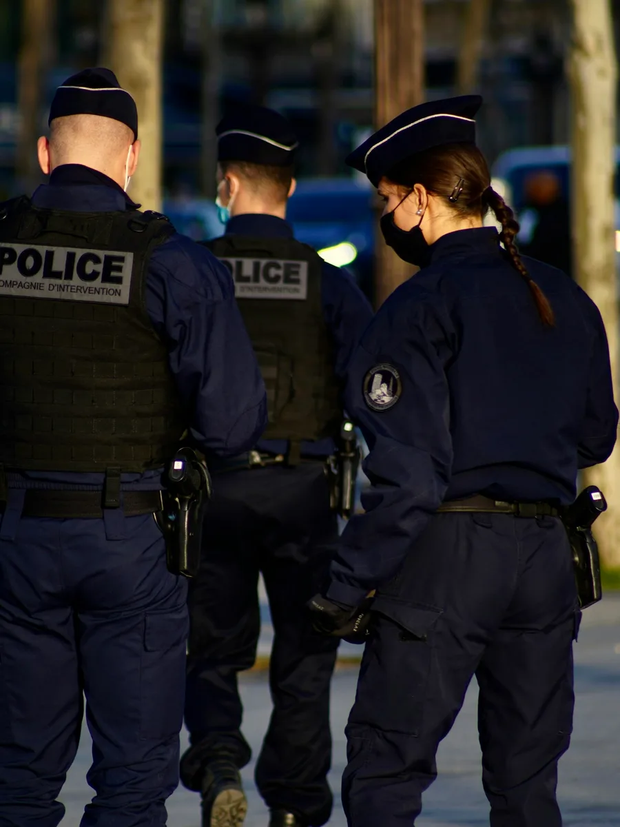 Trois policiers en uniforme, de dos, dans une rue le soir.