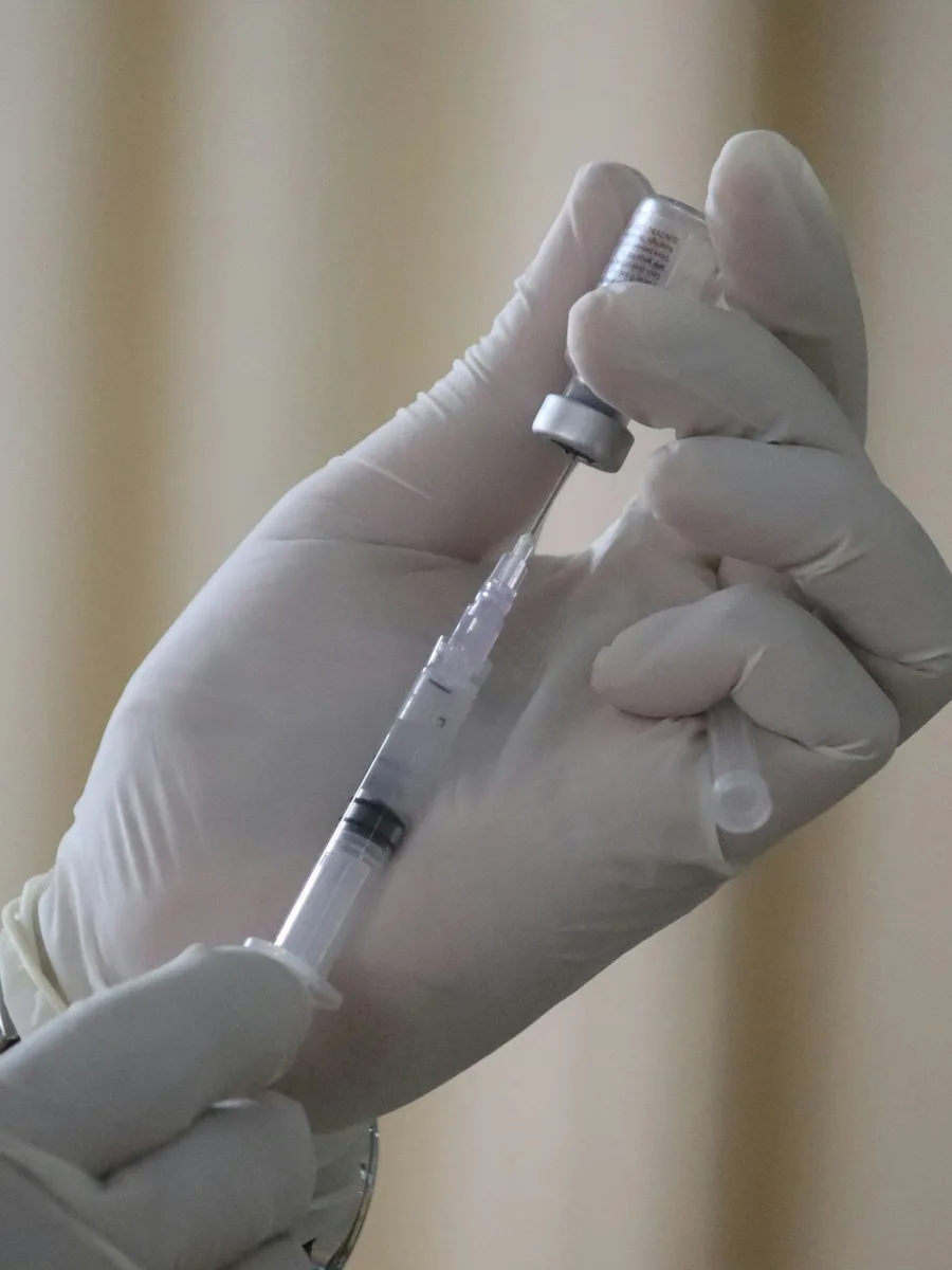 Des mains gantées prélèvent le contenu d'un flacon de vaccin avec une seringue.