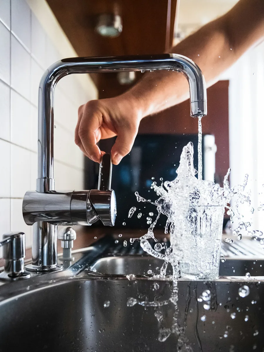 Une main ouvre un robinet de cuisine d'où coule l'eau