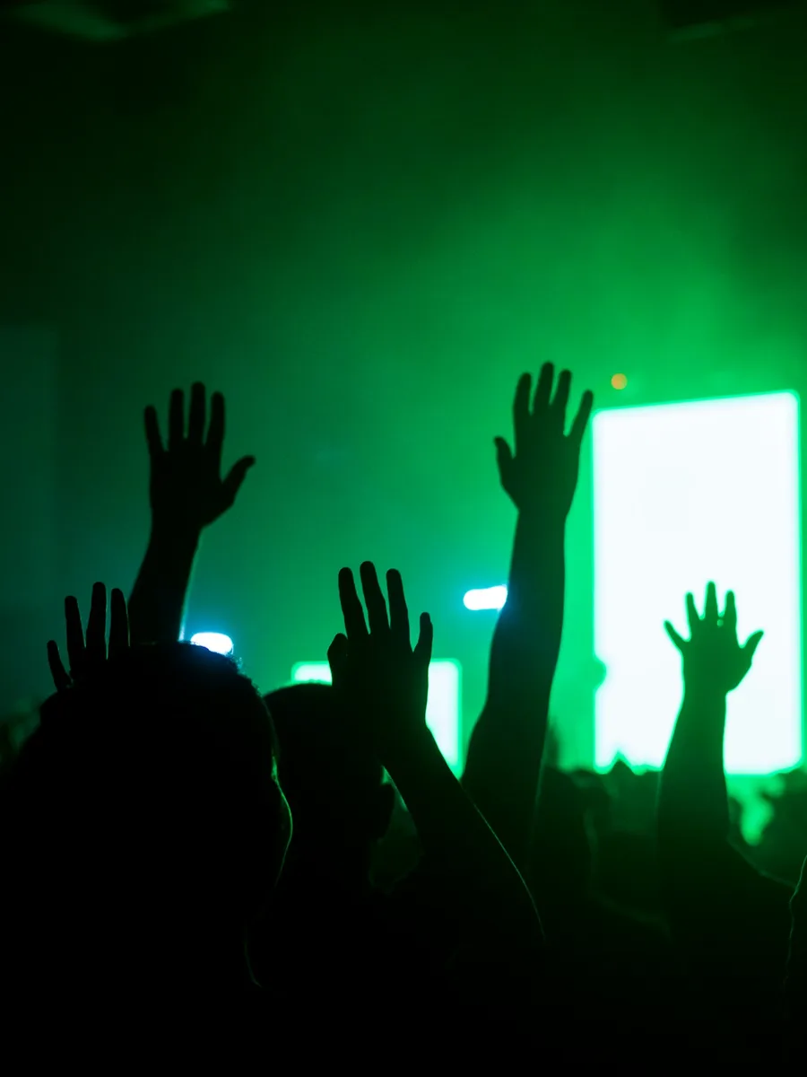 Des mains levées dans la foule d'un concert, sous des projecteurs verts
