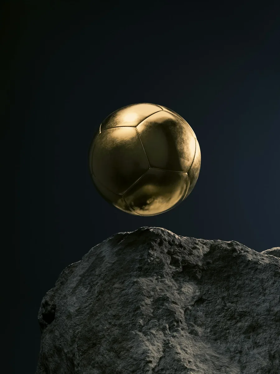 Un ballon de football doré posé sur un rocher, sur fond sombre