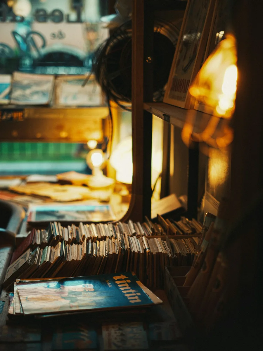 Des piles de livres et de revues anciennes sur les étagères d'une librairie faiblement éclairée.
