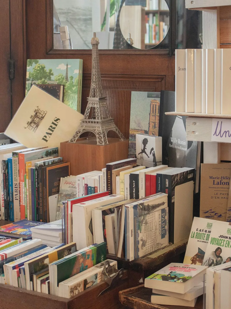 Des piles de livres sur une table de librairie, devant une petite tour Eiffel