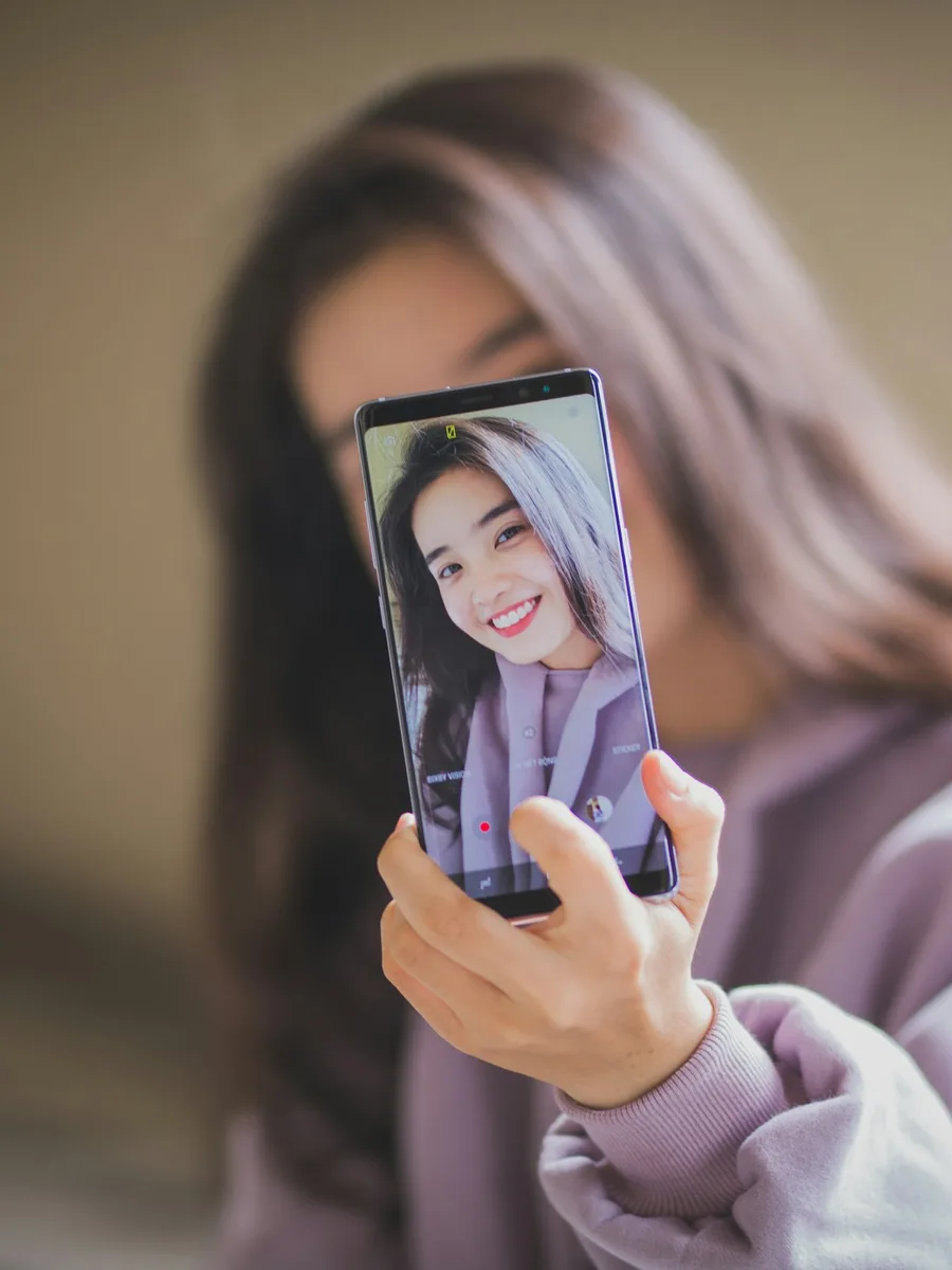 Une femme se prend en photo avec son smartphone, dont l'écran affiche son visage