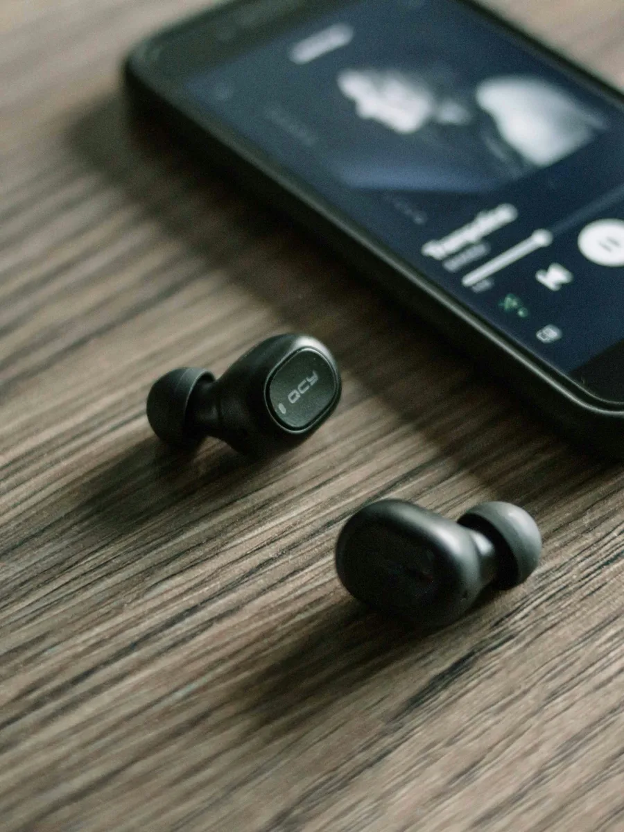 Des écouteurs sans fil posés sur une table à côté d'un smartphone qui lit de la musique