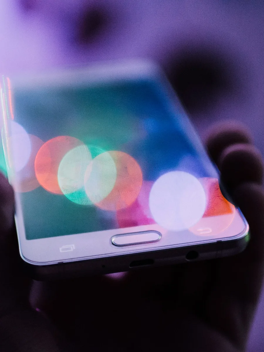 Une main tient un smartphone devant des lumières colorées floues