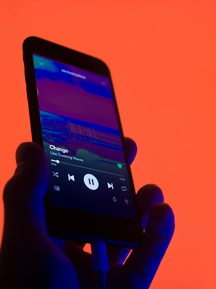 Une main tient un smartphone affichant un lecteur de musique, sur fond rouge et bleu