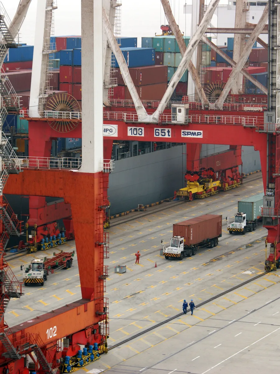 Des portiques rouges et des piles de conteneurs sur le terminal du port en eau profonde de Yangshan, à Shanghai, avec des camions qui circulent entre les quais.