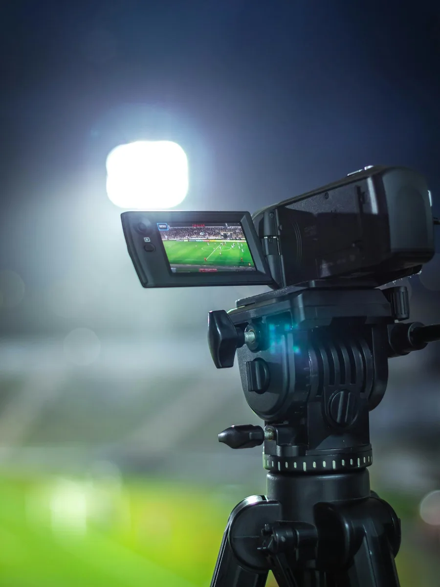Une caméra de télévision sur trépied filme un match de football de nuit, sous les projecteurs