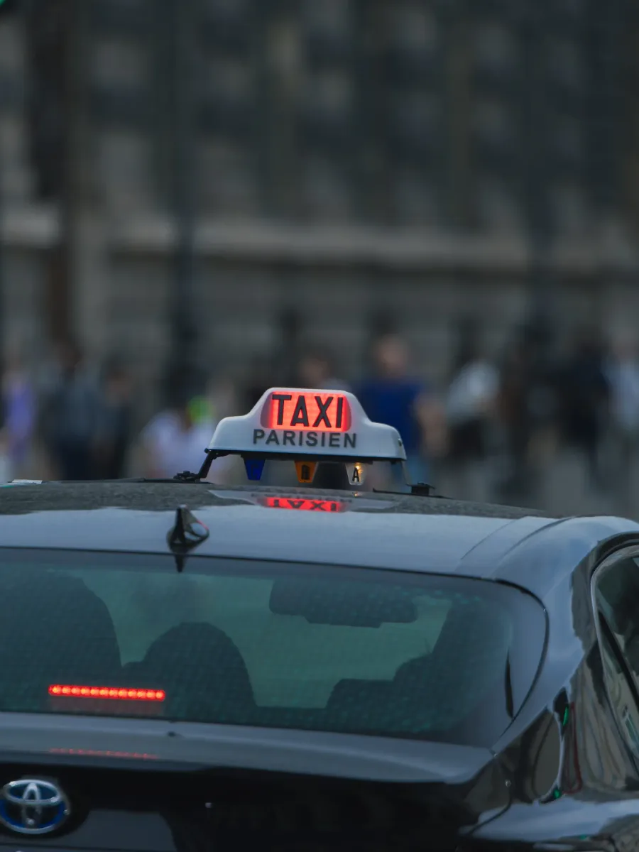 Le lumineux « Taxi » rouge sur le toit d'un taxi noir dans une rue parisienne, passants flous en arrière-plan