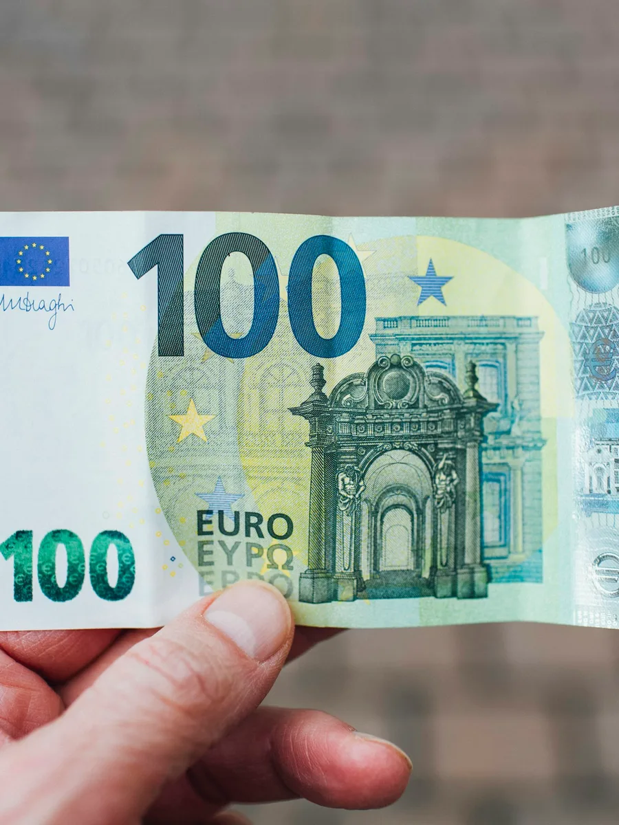 Une main tient un billet de 100 euros face à l'objectif