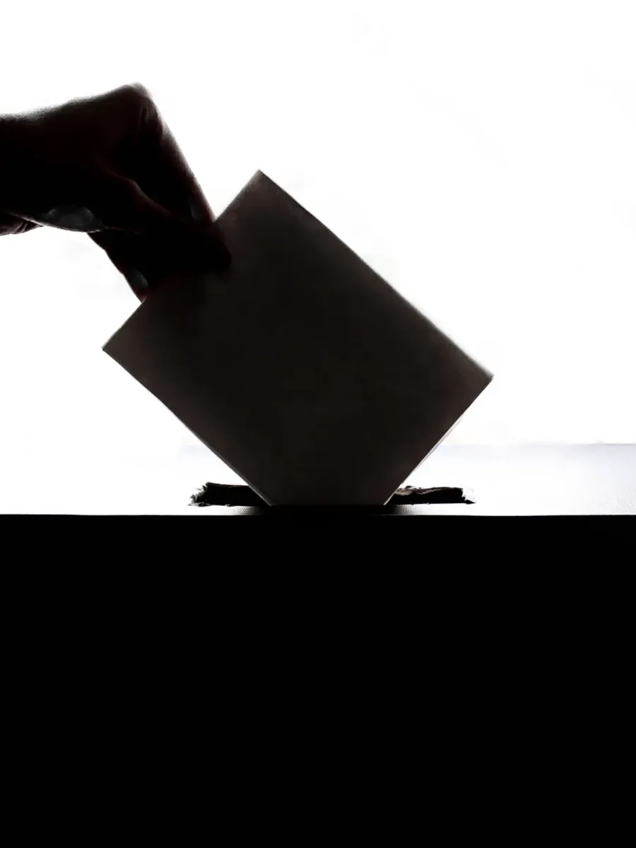 Silhouette d'une main glissant une enveloppe dans une urne