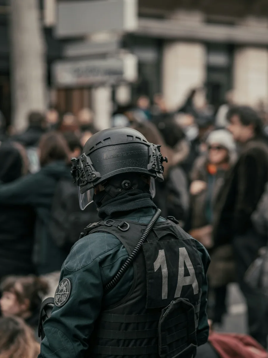 Policier casqué en tenue noire de dos, face à une foule à Paris