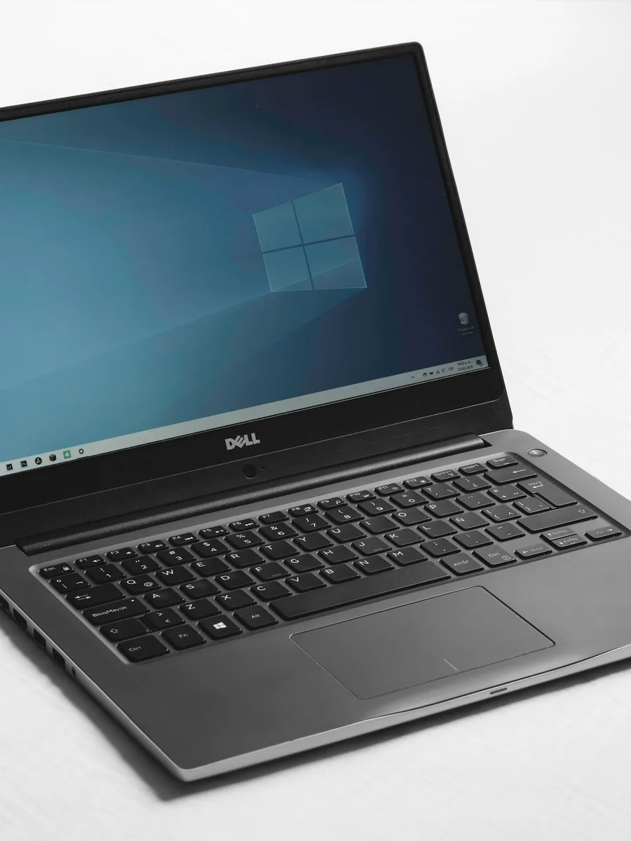 Un ordinateur portable ouvert, dont l'écran affiche le fond bleu et le logo de Windows, posé sur une surface blanche
