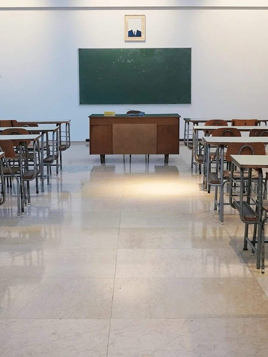 Salle de classe vide avec un tableau vert, un bureau et des rangées de tables (photo d’illustration).