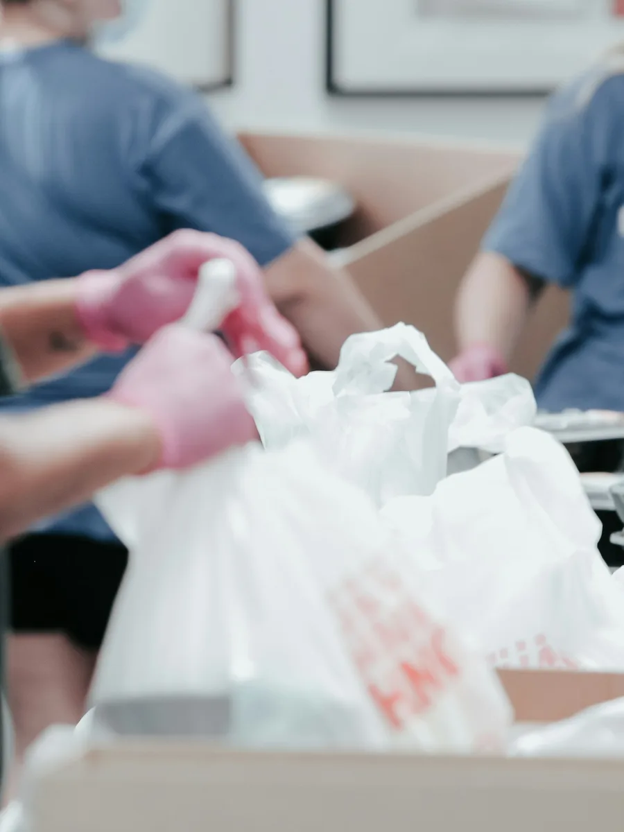 Des bénévoles en gants roses remplissent des sacs de denrées
