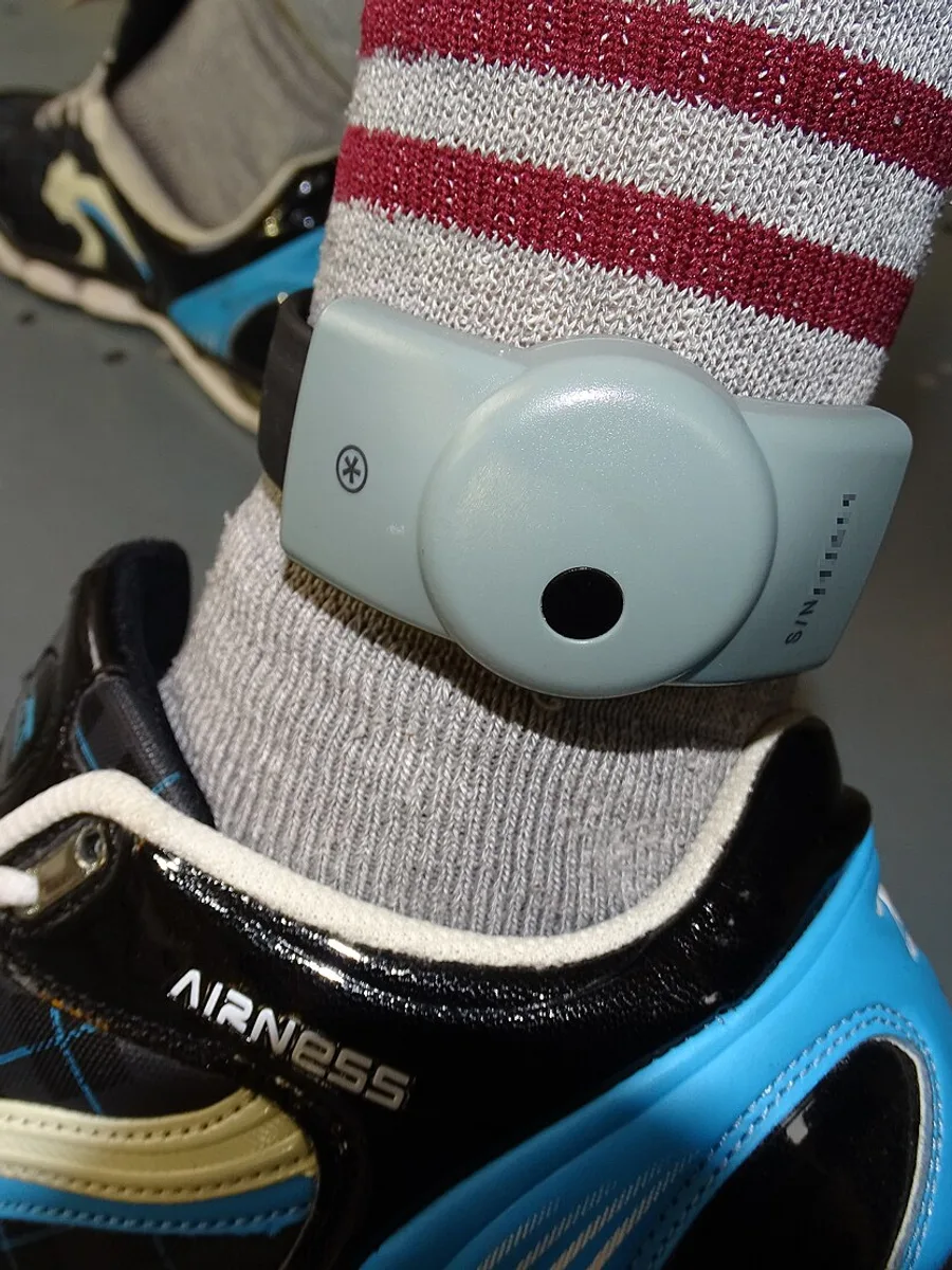 Un bracelet électronique de surveillance gris fixé à la cheville d'une personne, par-dessus une chaussette rayée