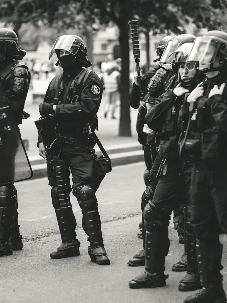 Des policiers casqués en tenue de maintien de l'ordre alignés dans une rue, en noir et blanc