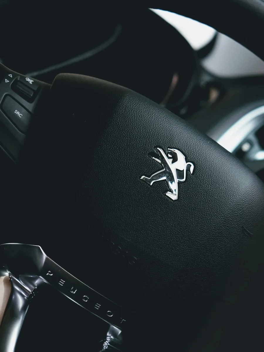 Gros plan sur un volant rond actuel de Peugeot, frappé du lion de la marque.