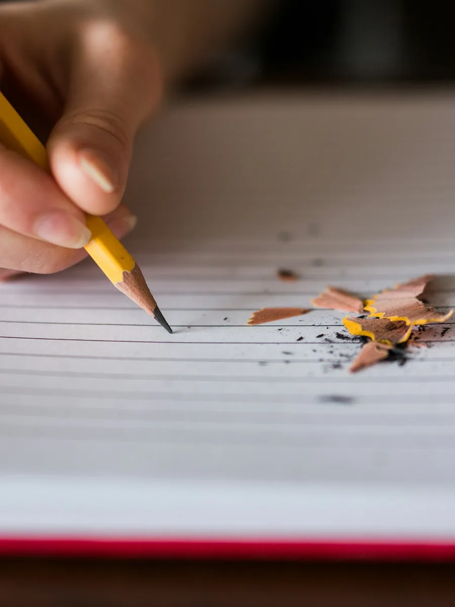 Gros plan d'une main qui écrit au crayon à papier sur une feuille.