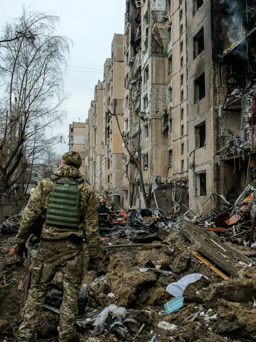 Un soldat en tenue de camouflage marche dans les décombres au pied d'immeubles détruits