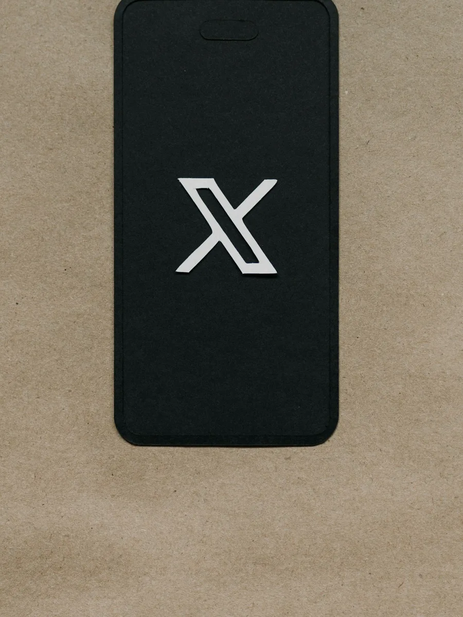 Smartphone noir posé sur un papier kraft, affichant le logo X du réseau social au centre de l'écran.