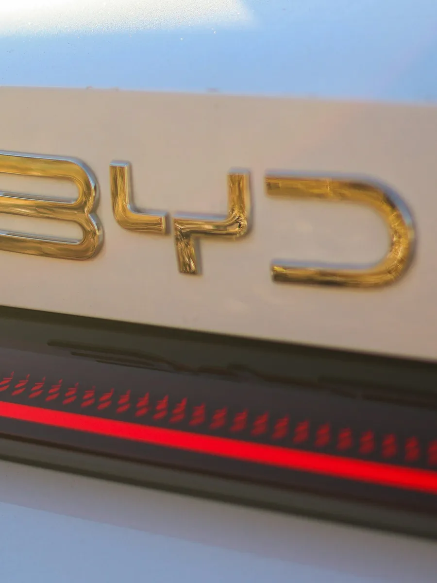 Gros plan sur le logo doré BYD à l'arrière d'une voiture blanche.