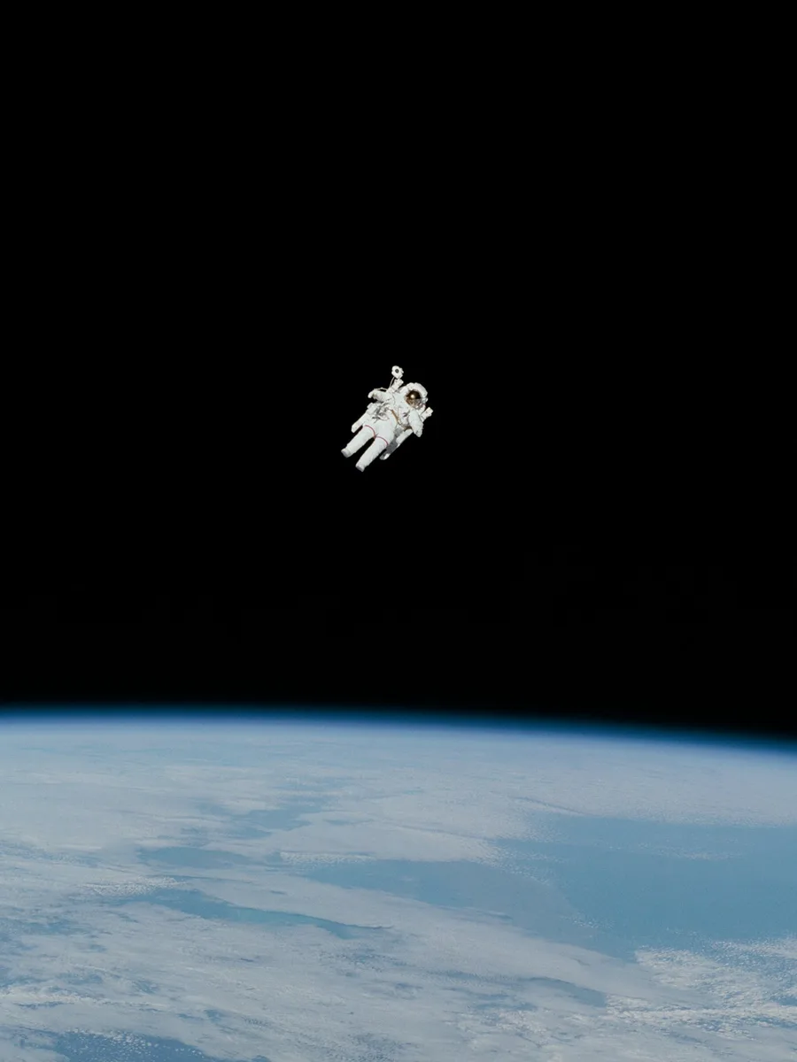 Un astronaute en combinaison blanche flotte dans le noir de l'espace au-dessus de la courbure de la Terre