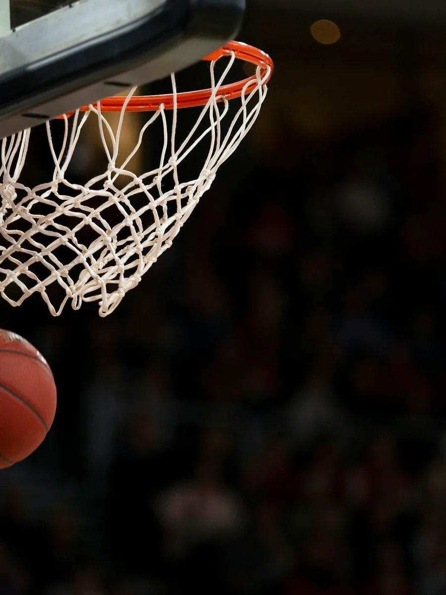 Un ballon de basket passe sous un panier, dans la pénombre