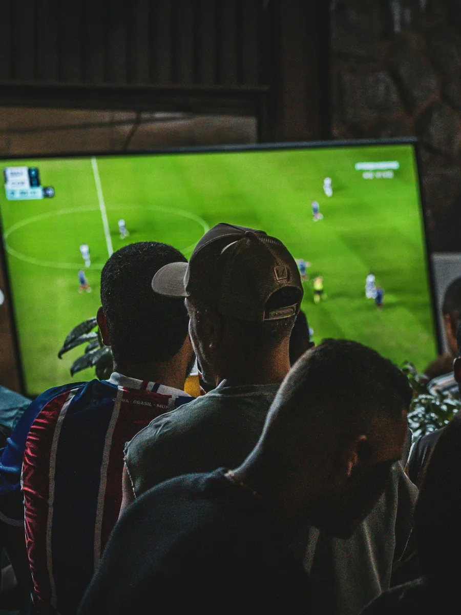 Un groupe de personnes de dos regarde un match de football sur un grand écran de télévision