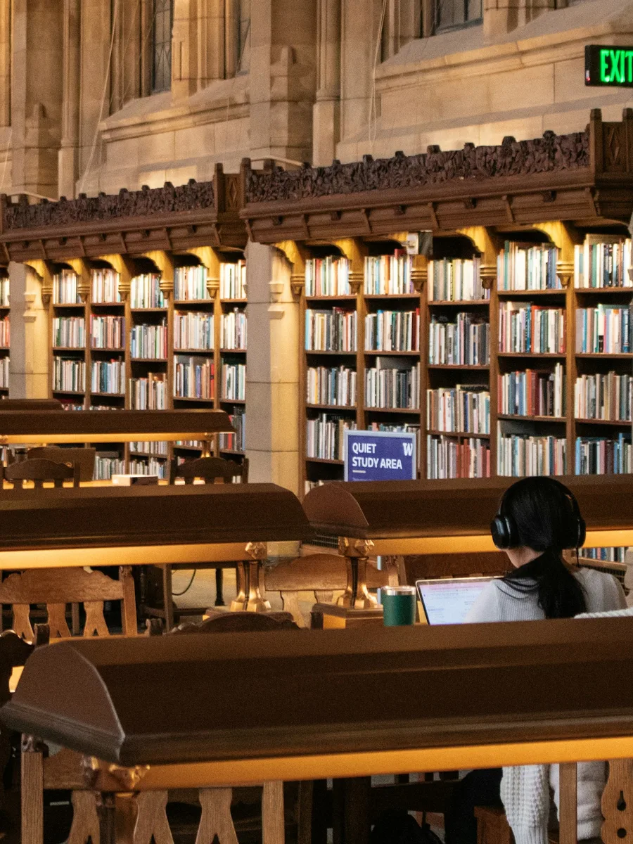 Une grande salle de bibliothèque universitaire ancienne, avec ses rayonnages de livres et une personne lisant à une table