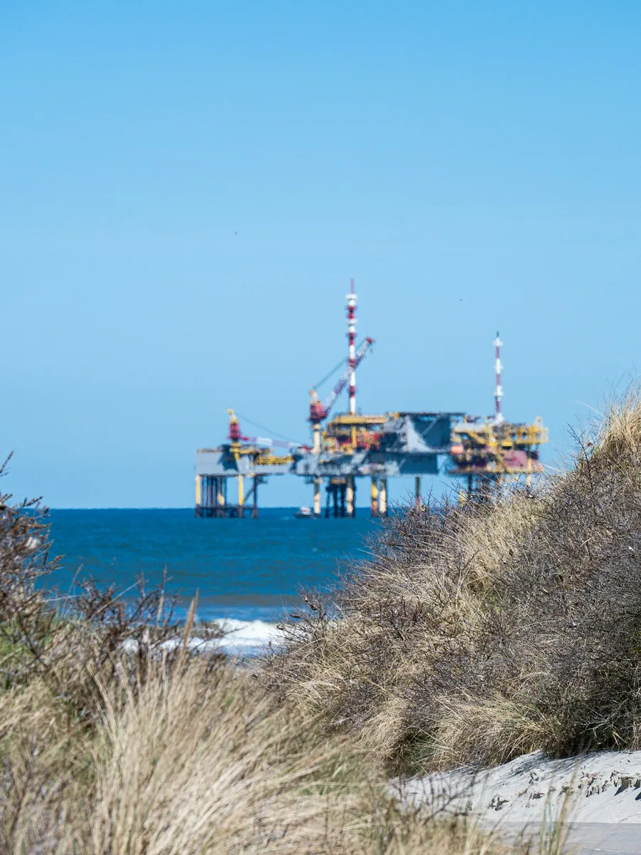 Une plateforme pétrolière et gazière en mer, vue depuis une plage bordée de dunes