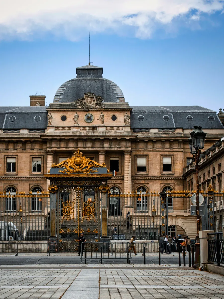 La façade et la grille dorée du Palais de justice de Paris, sur l'île de la Cité, sous un ciel nuageux