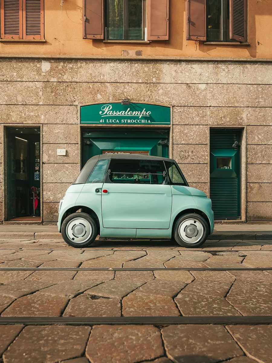 Une Fiat Topolino électrique bleu clair garée sur une rue pavée devant une boutique