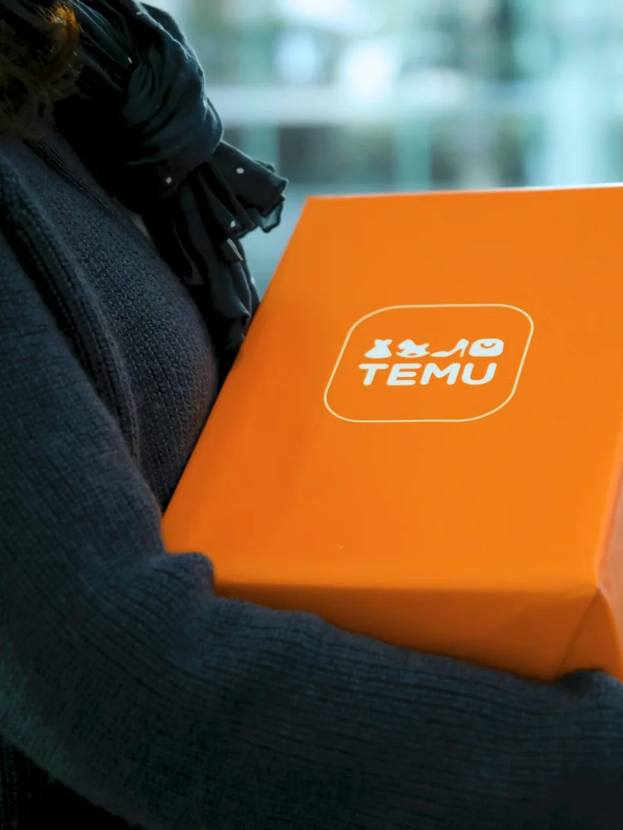 Une personne porte sous le bras un colis orange marqué du logo Temu