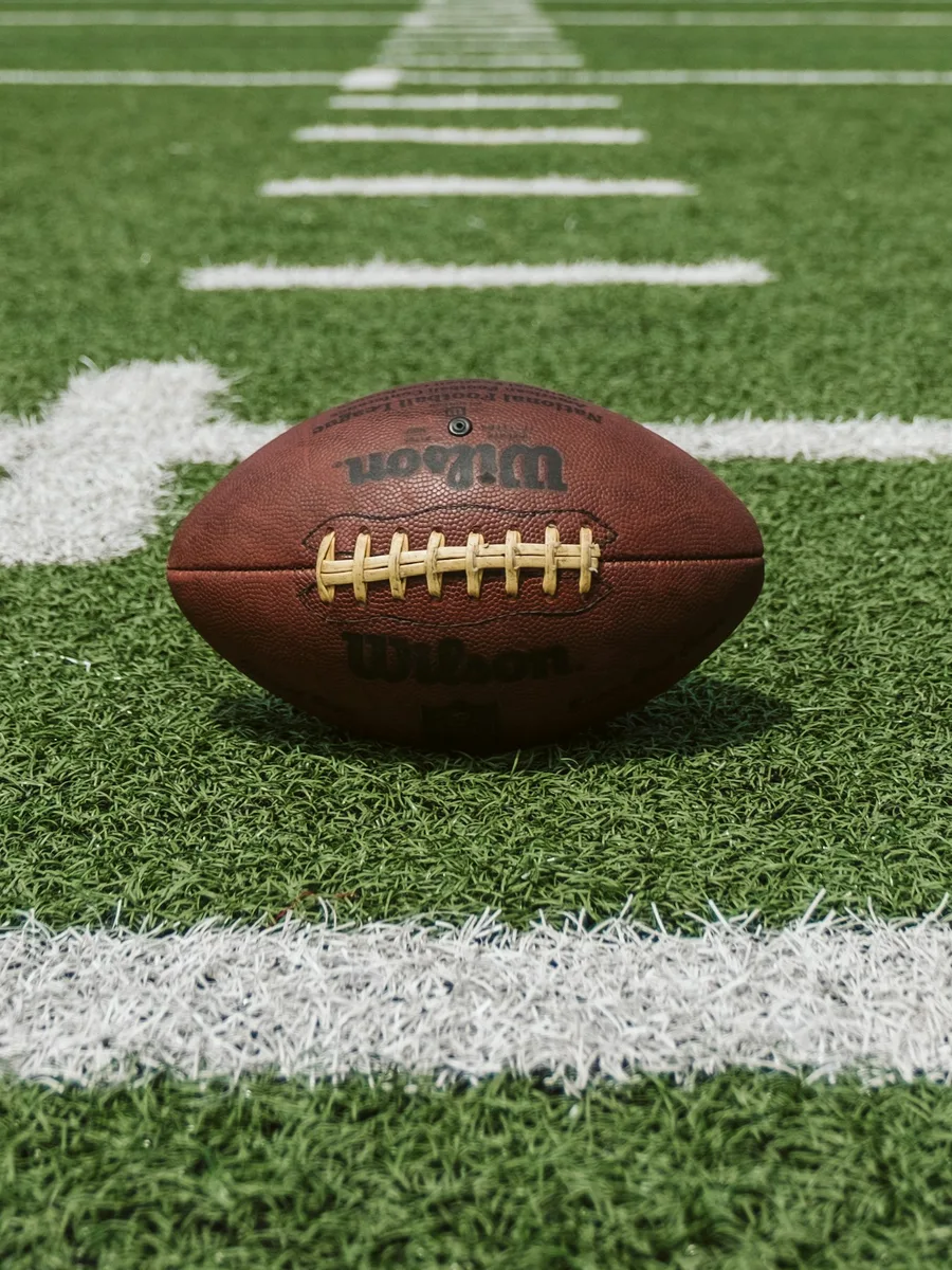 Un ballon de football américain posé sur la pelouse, près des lignes blanches du terrain