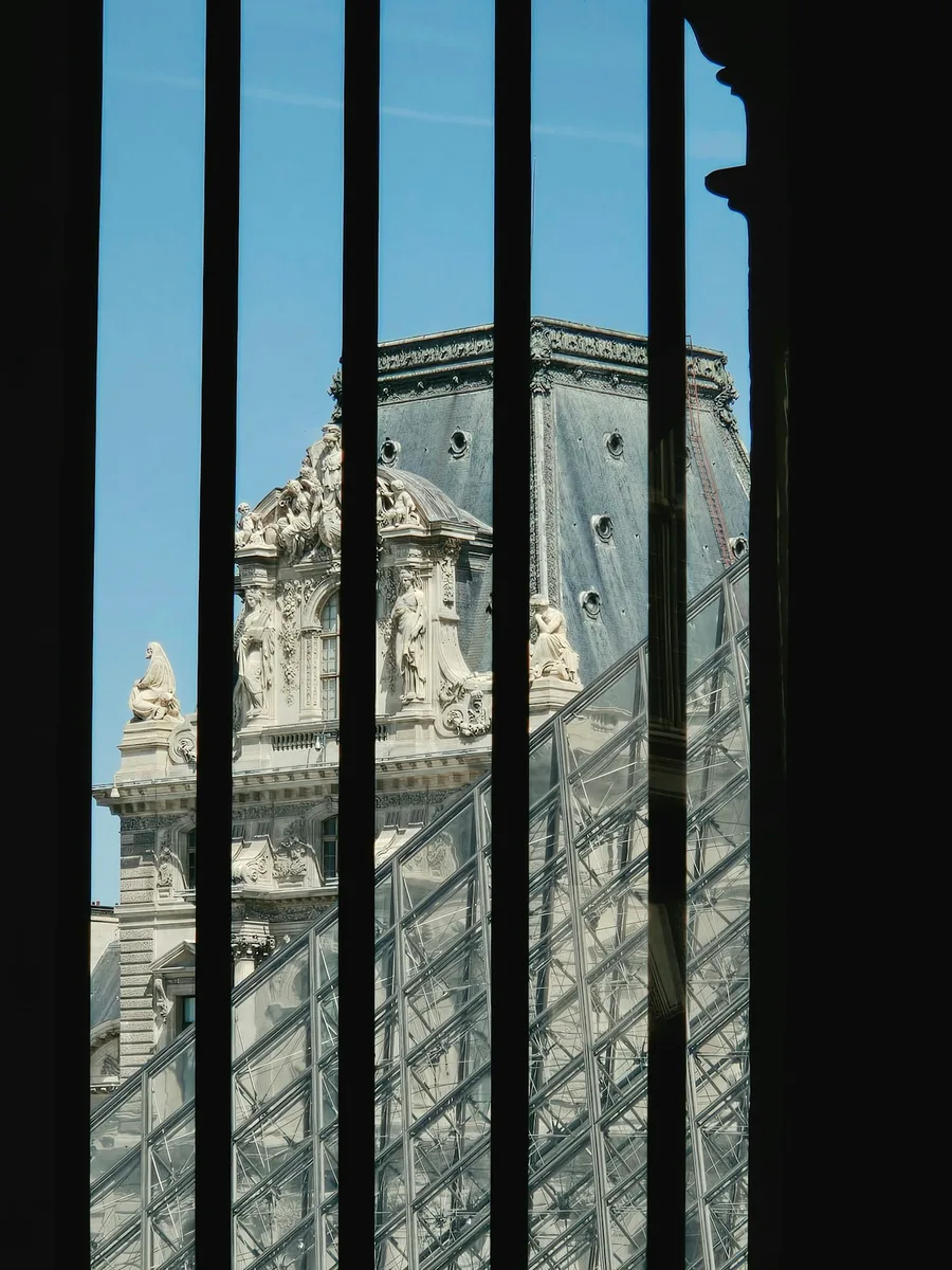 La pyramide et un pavillon du Louvre vus à travers des barreaux sombres