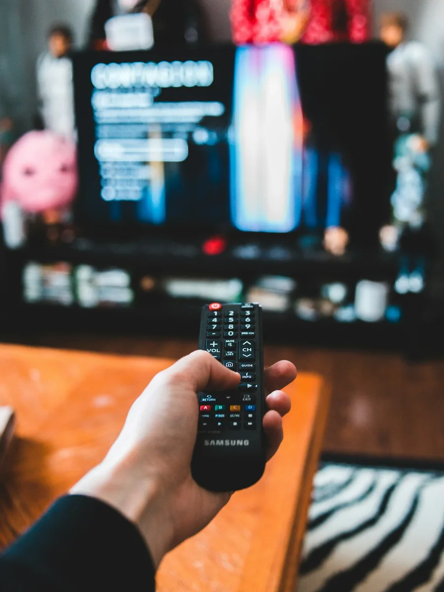 Une main tenant une télécommande devant un téléviseur allumé sur un menu de streaming